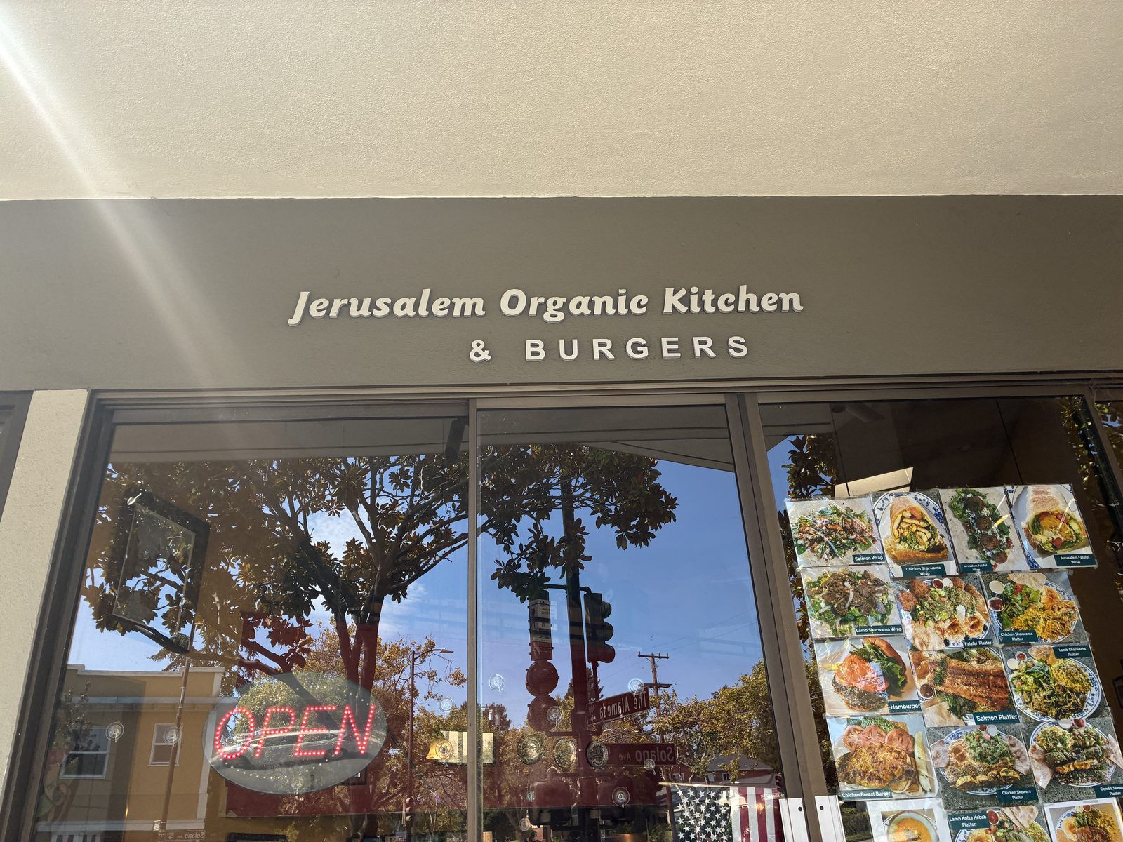 The window of a Jerusalem organic kitchen and burger shop, menu photos and an OPEN sign inside the glass