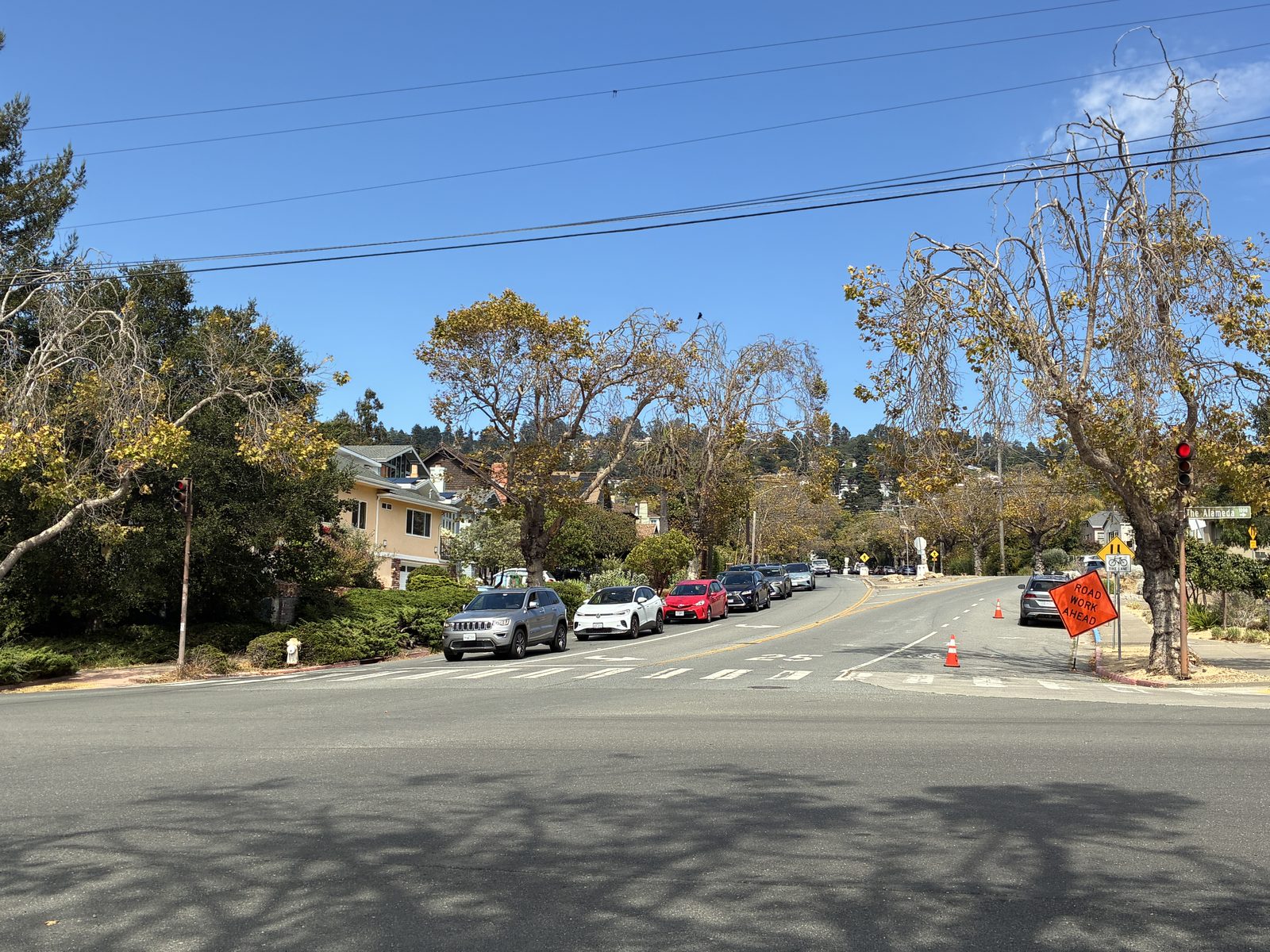 A residential crossroads, parked cars and trees just beginning to turn