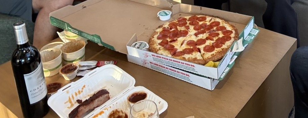 A pepperoni pizza in its box next to the takeout trays and the wine bottle