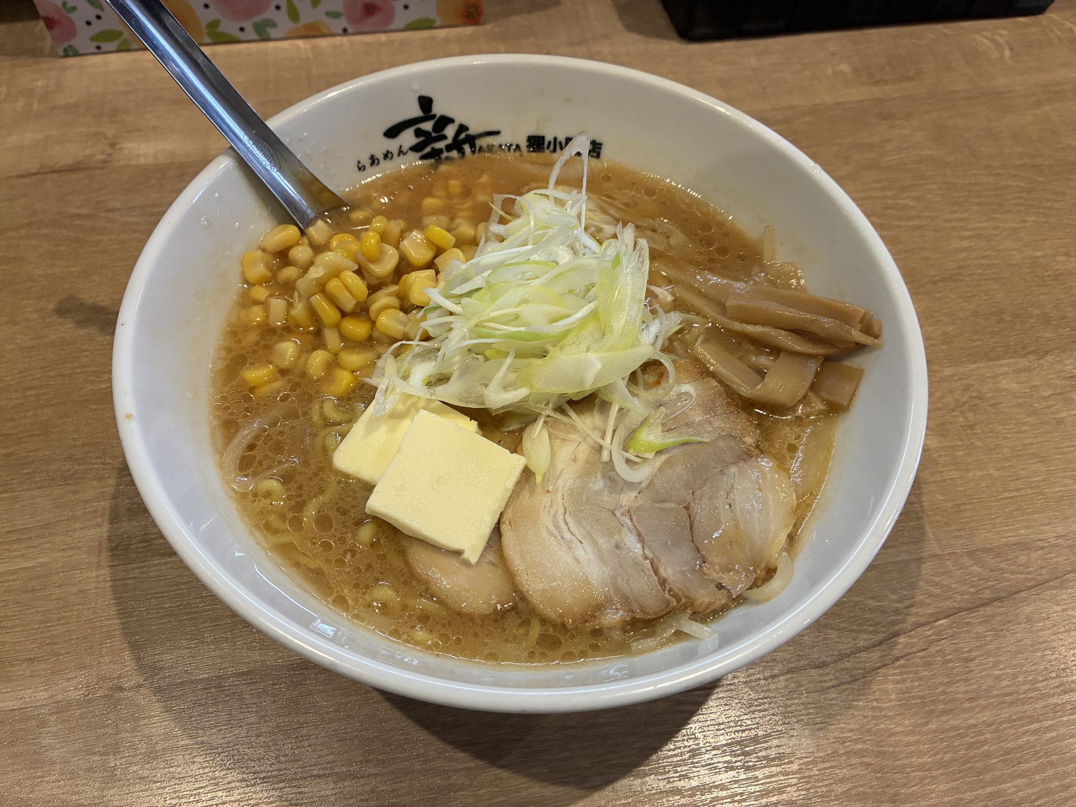 A bowl of miso ramen topped with sweetcorn, a pat of butter, chashu and white leek